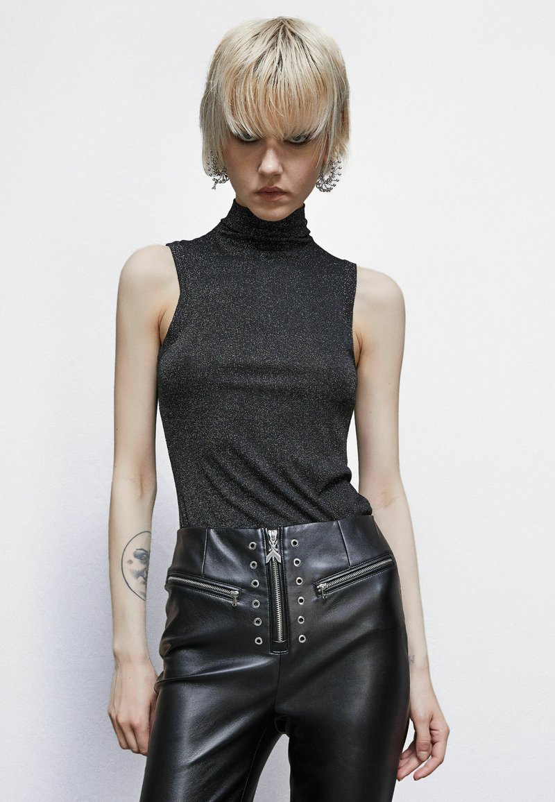 Top nero senza maniche con un collo alto e rigato, realizzato in tessuto luccicante. Abbinato a pantaloni in pelle neri a vita alta e slim con tasche con zip.