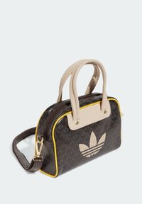 Borsa marrone con motivo a fantasia, manici beige e rifiniture gialle. Dotata di chiusura a cerniera e logo sulla parte frontale. Texture liscia, forma compatta.