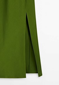 Détail d'une jupe en tissu vert avec une coupe droite et une fente à l'avant.