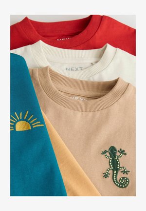 Drei T-Shirts übereinander gestapelt: ein rotes, ein cremfarbiges und ein türkisfarbenes mit gelber Sonnenstickerei, sowie ein beiges mit grüner Echsenstickerei auf dem unteren Shirt.