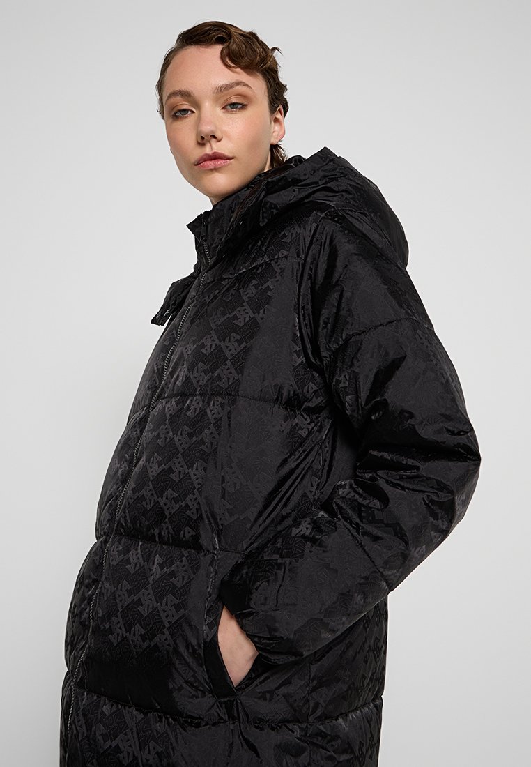 Schwarze Pufferjacke mit Kapuze, ausgestattet mit einem gesteppten Muster, glänzender Textur und einem Reißverschluss vorne. Sie verfügt über Seitentaschen und eine lockere Passform.