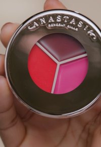 Ronde compacte met een spiegelende zilverkleurige buitenkant, met drie secties van romige lipkleur in rood, donkerroze en lichtroze.