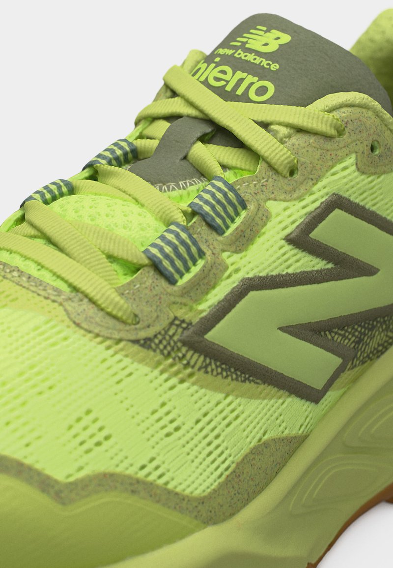 Primer plano de una zapatilla de correr New Balance verde neón con detalles caqui, cordones detallados y la marca "Fierro" en la lengüeta.