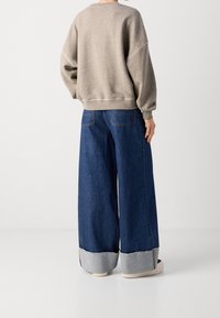 Sudadera gris oversize con hombros caídos, combinada con vaqueros de pierna ancha en azul que presentan un dobladillo en gris claro contrastante.