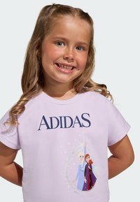 Fialové bavlnené tričko s trblietavým grafikou dvoch animovaných postáv z populárnej franšízy, nad ktorými je vytlačený nápis "ADIDAS".