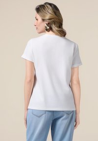 Camiseta blanca de manga corta con cuello redondo, hecha de una tela suave. Combinada con pantalones de color azul claro, muestra un diseño simple y limpio.