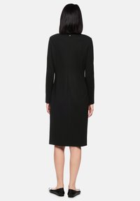 Schwarzes, langärmeliges Kleid mit figurbetonter Silhouette, knielang und mit einer Rückennaht-Detail. Glatter Stoff und minimalistisches Design.