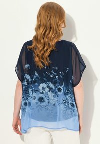 Navy blauer Chiffon-Top mit lockerer Passform, das ein florales Muster in schattierten Blautönen zeigt, mit einem sanften, durchsichtigen Abschluss an den Ärmeln und dem Saum.
