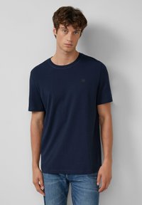 Camiseta de algodón azul marino con mangas cortas, cuello redondo y un sutil detalle del logo en el lado izquierdo del pecho. Textura suave, corte relajado.