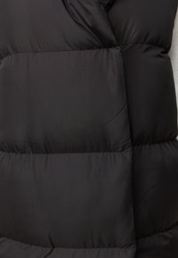 Schwarze Steppweste mit quiltetem Muster, glatter Textur und hohem Kragen. Verfügt über ein überlappendes Frontpanel-Design und ist isoliert für Wärme.