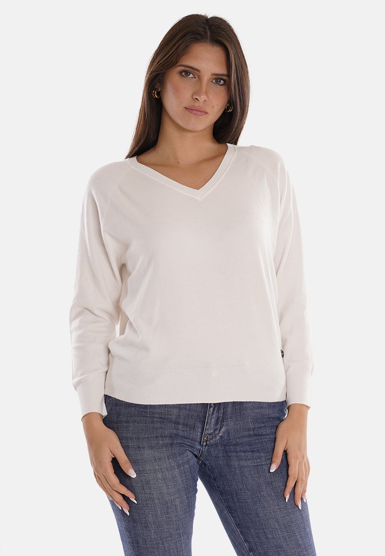 Maglione bianco con scollo a V realizzato in un materiale morbido, con maniche lunghe e un fit rilassato, abbinato a jeans skinny blu scuro.