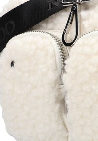 Witte pluche tas met een zachte, gestructureerde oppervlakte, ritssluiting en metalen hardware. Beschikt over een zwarte schouderband met tekstdetails en een clip.