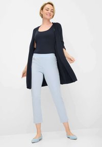 Marineblauwe cardigan, aansluitend marineblauw tanktop, lichtblauwe enkelbroek en lichtblauwe ballerina's. De cardigan heeft open mouwen en een gestructureerde afwerking.