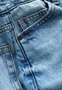 Gaiši zili džinsi ar priekšējo kabatu, kontrastējošām vīlēm un metāla pogas detaļu. Audumam ir mīksta tekstūra un viegla izbalēšana.