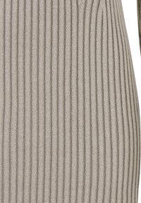 Tissu en maille côtelée beige avec des lignes verticales et un motif texturé, montrant un gros plan de la zone du torse d'un vêtement.