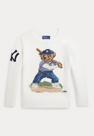 Pulover alb tricotat cu un urs îmbrăcat într-un echipament de baseball care ține o bâta, stând pe un teren, și un logo navy pe mâneca stângă.