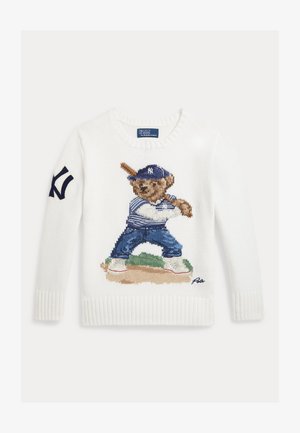 Hvit strikkegenser med en bjørn i baseballuniform som holder en balltre, stående på en bane, og en marineblå logo på venstre erme.