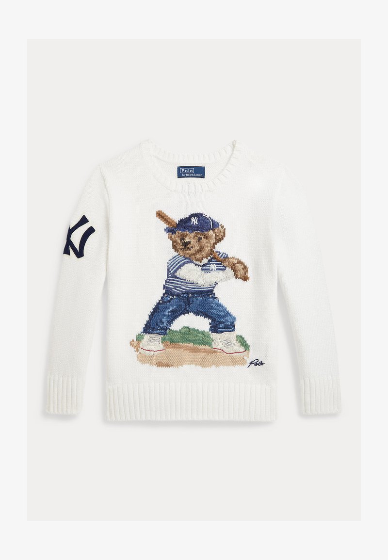 Bela pletena majica z risbo medveda v bejzbolski uniformi, ki drži lopar in stoji na igrišču, ter mornarsko moder logotip na levi rokavu.