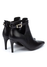 Botas de tobillo de cuero negro con punta afilada, un alto tacón de aguja y un detalle de correa con hebilla alrededor del tobillo. Textura suave.