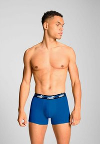 Blue fitted boxer shorts made of stretch fabric, featuring a black waistband with white "Puma" logo. Smooth texture and snug design.
