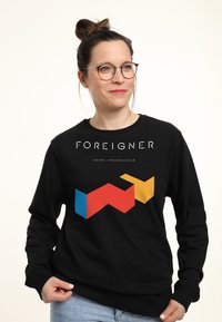 Felpa nera con un design geometrico che presenta forme rosse, blu e gialle. Il testo sopra dice "FOREIGNER" in bianco. Vestibilità casual.