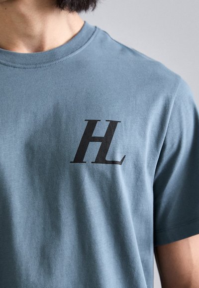 Ljusblå bomulls t-shirt med en svart "H" logotyp på vänster bröst. Rundhalsad design med korta ärmar, mjuk textur.