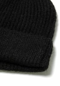 Bonnet tricoté noir avec une texture côtelée et un revers replié. Le matériau semble être en laine et doux, montrant une légère peluchure.