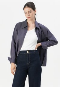 Chemise à rayures violette foncée avec des lignes bleues, associée à un jean en denim sombre taille haute avec des détails et des coutures en ton doré.