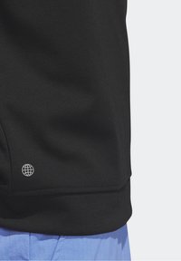 Tissu noir avec petit logo globe blanc près de l'ourlet, associé à un pantalon texturé bleu clair.