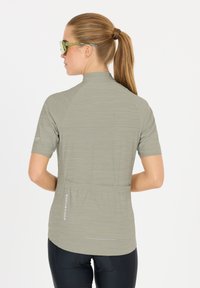 T-shirt de sport gris clair à manches courtes avec un col montant, tissu texturé et une poche arrière avec "ENDURANCE" imprimé verticalement.