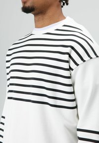 Witte sweatshirt met horizontale zwarte strepen, ronde halslijn en zachte stoftextuur. Ontworpen met een relaxte pasvorm.