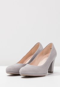 Talons hauts en daim gris avec un bout arrondi, une texture lisse et un talon bloc de hauteur intermédiaire. Accent de couture subtile sur la tige.