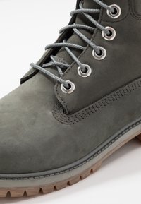 Šedé semišové kotníkové boty se šedými tkaničkami, kovovými otvory a texturovanou gumovou podrážkou. Disponují úhledným prošitím podél okrajů a podporující konstrukcí.