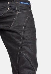 Jean en denim noir avec des coutures blanches contrastantes, cinq poches et quincaillerie en métal. Le design comprend des jambes fuselées et des coutures détaillées.