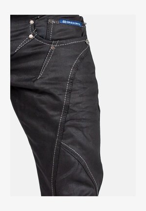 Jean en denim noir avec des coutures blanches contrastantes, cinq poches et quincaillerie en métal. Le design comprend des jambes fuselées et des coutures détaillées.