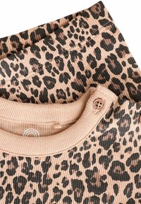 Ljust brunt ribbat linne med leopardmönster i svart och tan. Har en rund halsringning och en knappdetalj. Mjuk textur.