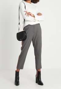 Harmaat housut, joissa on oranssit sivuraidat, yhdistettynä valkoiseen tekstuuripaitaan. Musta laukku, jossa on niittejä ja korolliset nilkkurit.