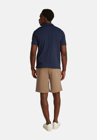 Camisa polo azul marino, de manga corta, con corte relajado, combinada con pantalones cortos beige y zapatillas blancas. Textura suave, diseño sencillo.