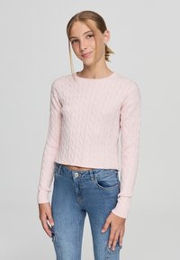 Maglione corto a treccia rosa con maniche lunghe, dotato di scollo rotondo. Abbinato a jeans in denim blu, con una vestibilità comoda.