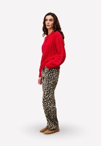 Un pull en tricot rouge, un pantalon beige à imprimé léopard et des chaussons marron. La tenue présente un tissu texturé avec une coupe décontractée.