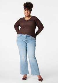 Bruin, gestructureerd, langharig shirt gecombineerd met lichtblauwe uitlopende spijkerbroek. Opvallende details zijn een ronde halslijn en versierde bruine schoenen.