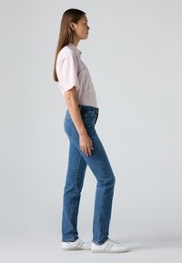 Pink and white striped short-sleeve shirt, blue jeans, and white sneakers; side view showcases the fitted silhouette and color contrast.
