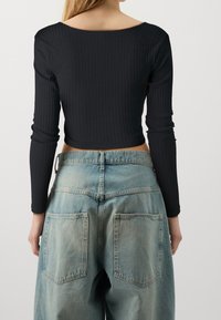 Black ribbed long-sleeve crop top viewed from the back, paired with faded blue wide-leg jeans featuring large rear pockets.