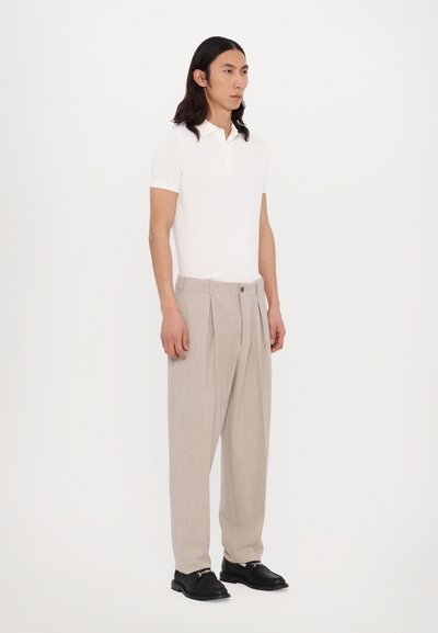 Polo shirt blanc à manches courtes, pantalon beige plissé et chaussures noires. Tissu lisse, coupe décontractée et design ajusté avec une fermeture à boutons.