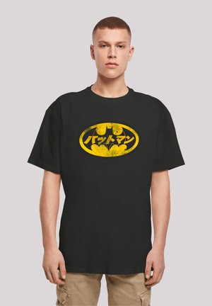 Black T-shirt featuring a yellow distressed Batman logo with Japanese characters. Short sleeves and a relaxed fit. Classic cotton material.