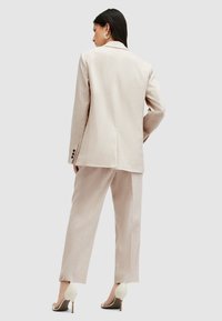 Lichtbeige pak met een op maat gemaakte blazer en rechte broek. De stof heeft een subtiele textuur, en de outfit is gecombineerd met crèmekleurige hoge hakken.