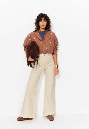 Chemise brune rayée avec des accents floraux, pantalon large beige, sac frangé en suédine marron et chaussures à imprimé animal marron.