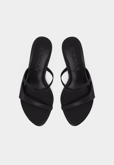 Paire de sandales noires ouvertes à bout ouvert, à enfiler, avec des lanières fines croisées et une semelle plate sur fond blanc.