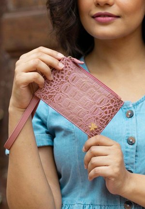 Lichtroze portemonnee met krokodillenstructuur, ritssluiting en polsband. Bevat een kleine gouden bloemenaccent. Gladde leren materiaal.