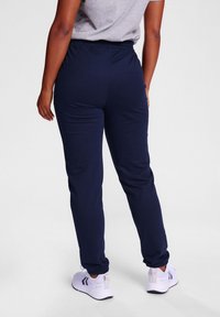 Marineblaue Jogginghosen mit elastischem Bund und schmal zulaufenden Beinen, aus glattem Stoff gefertigt. Kombiniert mit weißen Sportschuhen.